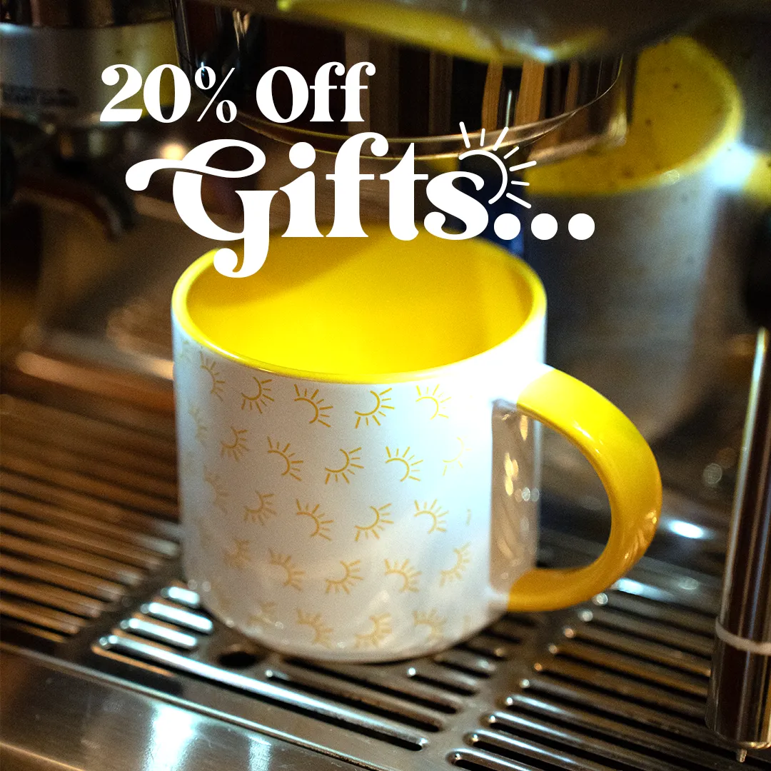 Yellow and white ceramic mug with sun patterns placed under an espresso machine dispensing coffee.