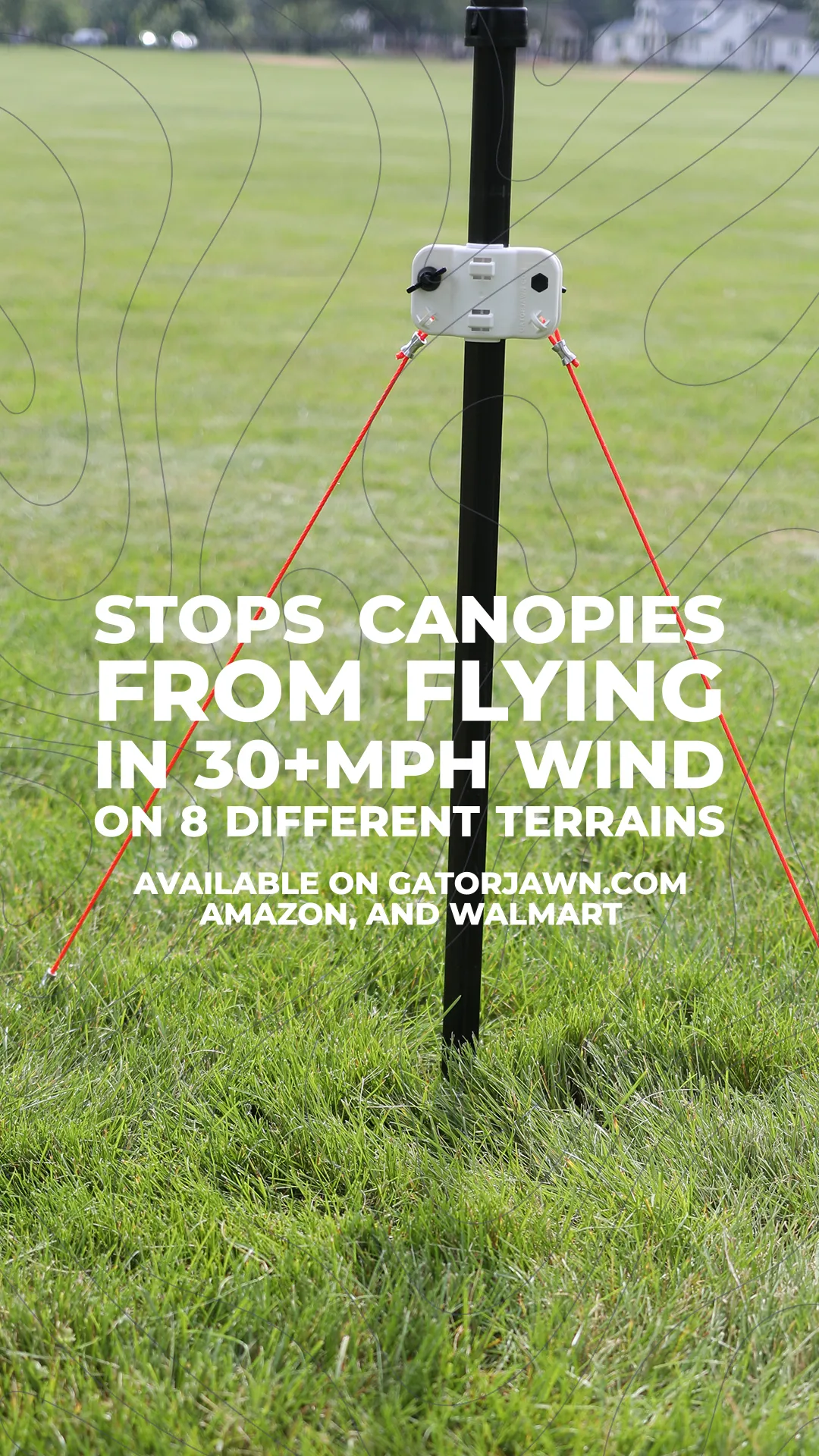 Close-up of a black stake with a white locking device holding two red cords stretched into green grass, with text about stopping canopies from flying in strong wind.