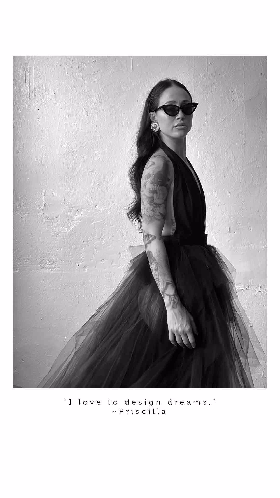 Black and white portrait of a woman with long hair, tattoos, wearing cat-eye sunglasses, large earrings, and a flowing tulle dress, with quote below saying 'I love to design dreams.' by Priscilla.